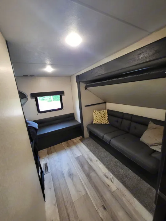 RV rental interior featuring a modern living space with dark sofa, window seating, and bunk beds. Ideal for travel comfort.. KZ Sportsmen SE 332bkhse 2022