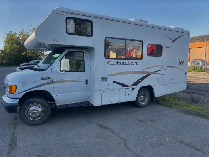 A white Winnebago Chalet Class C rv rental, a Ford E-350 motorhome, parked on asphalt with large windows and tan graphics.. Winnebago Chalet 2007