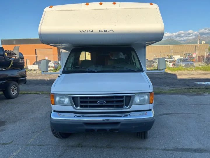 Front view of a white Ford RV camper van, ideal for an rv rental. It's parked on asphalt with mountains in the distance.. Winnebago Chalet 2007