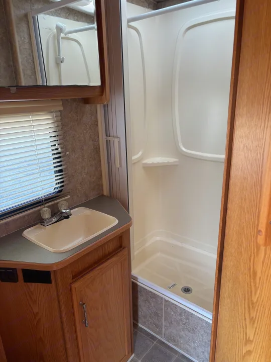 Compact RV rental bathroom with a sink, mirror reflecting the shower, and a clean, functional shower stall. Ideal for travel.. Winnebago Chalet 2007