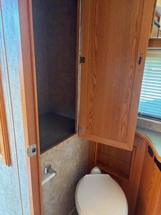 RV rental bathroom: Compact space featuring a toilet, open wood cabinets, and built-in storage.. Winnebago Chalet 2007