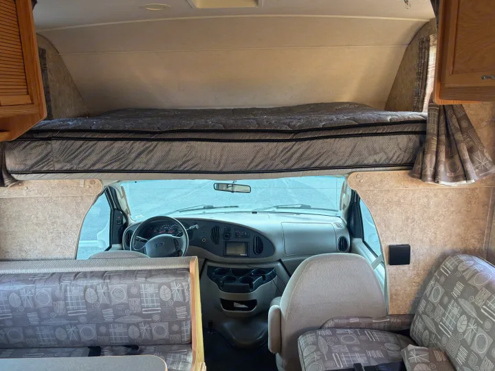 RV rental interior: driver's cab, spacious overhead bed, and patterned dinette. A cozy and functional camper space.. Winnebago Chalet 2007