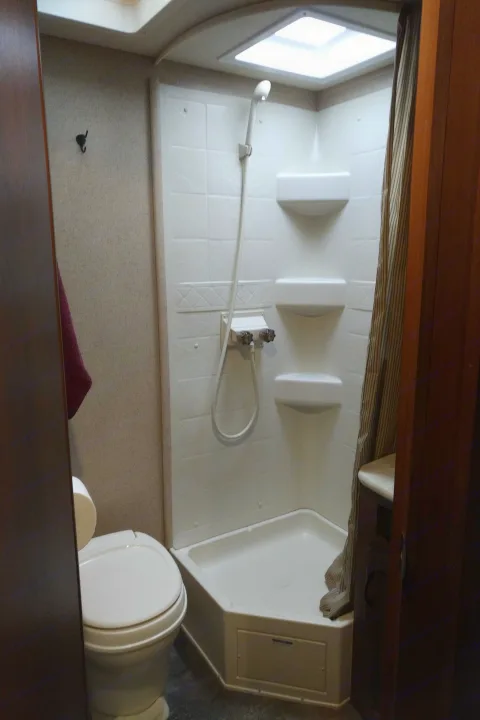 Clean and functional RV rental bathroom featuring a corner shower, toilet, and overhead skylight.. Other Other 2015