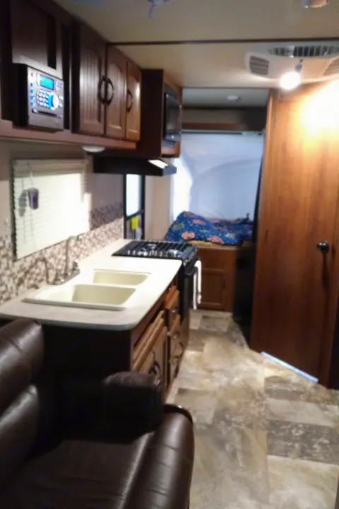 Cozy RV rental interior featuring a kitchen with sink, stove, overhead cabinets, living area sofa, and a rear bed.. Other Other 2015