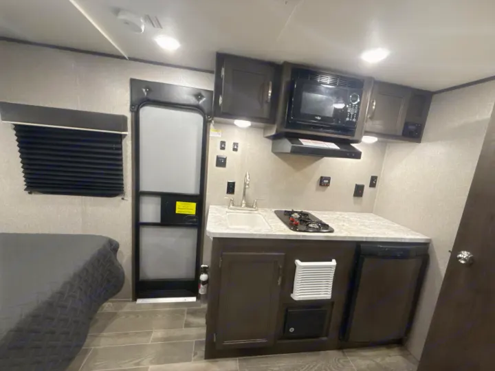 This rv rental offers a compact kitchen with sink, stove, microwave, cabinets, and a bed area for comfortable stays.. Jayco Jay Flight SLX 2021
