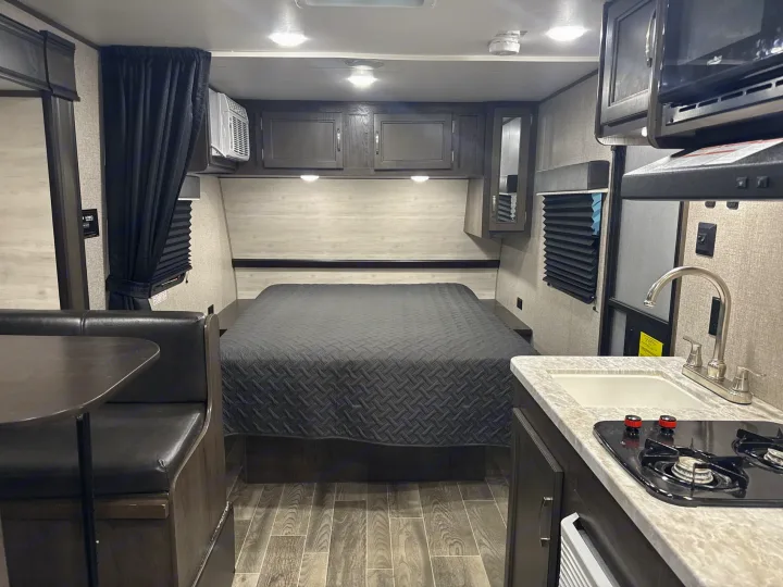 Interior of a modern rv rental featuring a comfortable bed, dinette, and kitchen with sink and stove, all in a compact, stylish design.. Jayco Jay Flight SLX 2021