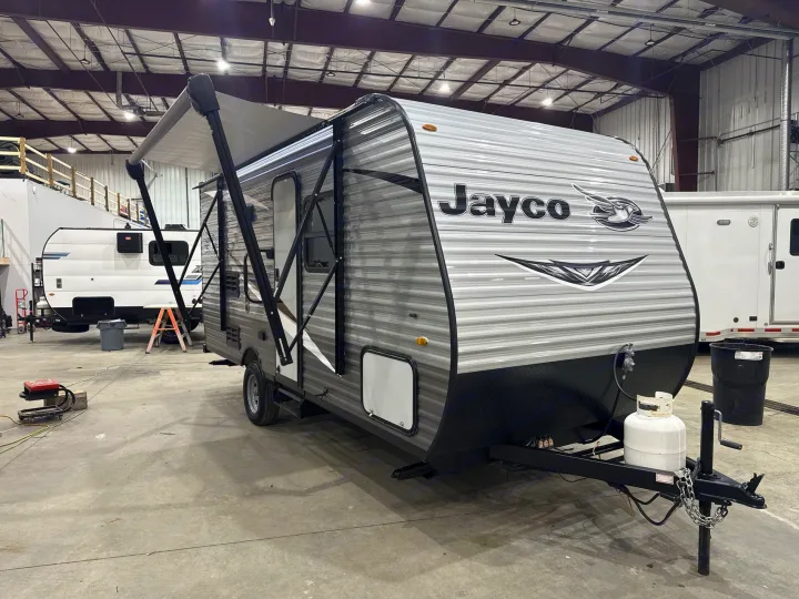 Grey Jayco travel trailer, awning extended, perfect for RV rental. Seen inside a service bay with other trailers.. Jayco Jay Flight SLX 2021