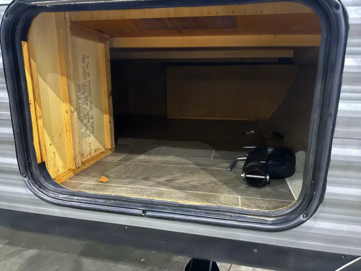RV rental's exterior storage bay, featuring unfinished wood, grey vinyl floor, and a black RV sewer hose connection part.. Jayco Jay Flight SLX 2021