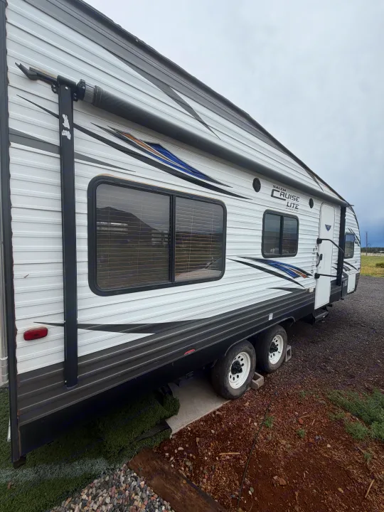 White and gray Salem Cruise Lite RV rental, featuring an awning and windows, parked on dirt/gravel under a cloudy sky.. Forest River Salem Cruise Lite 2018