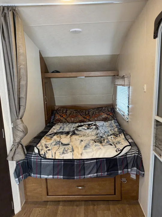 Cozy RV rental bedroom featuring a bed with a wolf blanket, camouflage pillow, and built-in storage. Ideal for travel adventures.. Forest River Salem Cruise Lite 2018