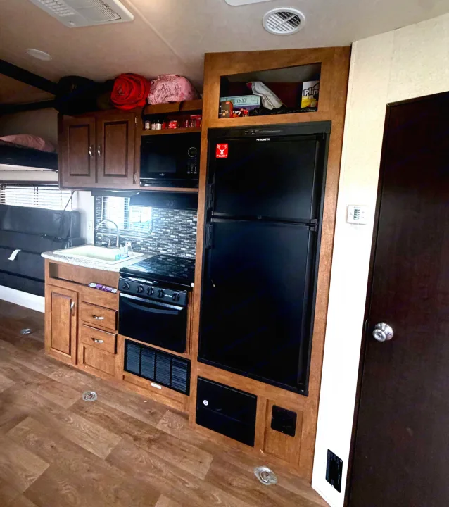 An RV rental interior showcasing a kitchen galley with Dometic fridge, stove, microwave, sink, cabinets, and bunk beds.. Forest River Salem Cruise Lite 2018