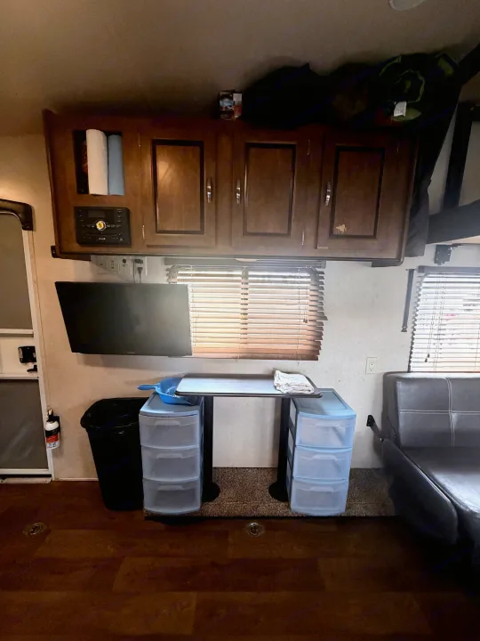 This RV rental interior features wood cabinets, a wall-mounted TV, a table with storage, a sofa, and windows with blinds.. Forest River Salem Cruise Lite 2018