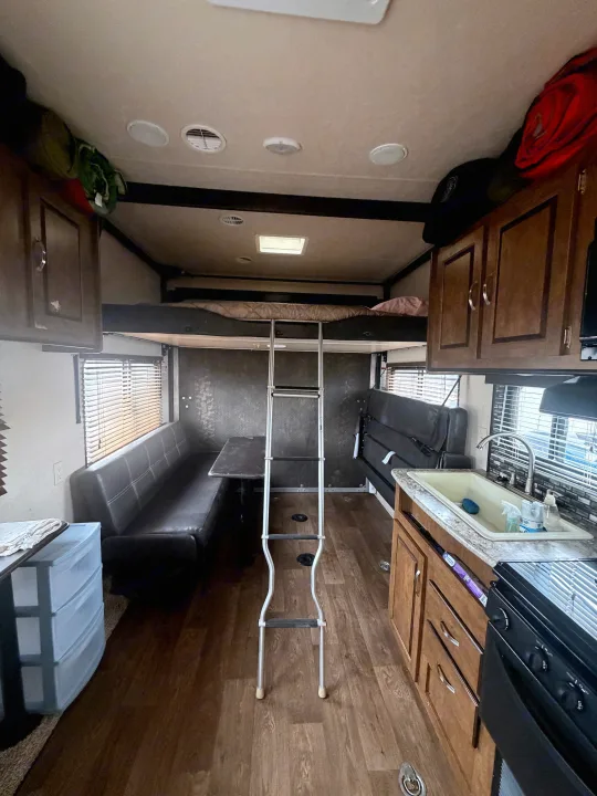 This RV rental interior features a kitchen with a sink & stove, a dinette seating area, and bunk beds with a ladder.. Forest River Salem Cruise Lite 2018