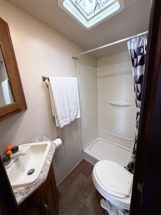 RV rental bathroom featuring a sink, toilet, and shower stall with checkered curtain. Compact and functional space.. Forest River Salem Cruise Lite 2018