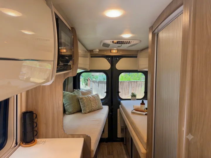 Modern RV rental interior showing a compact kitchen with microwave, and comfortable sleeping/seating areas with bright decor.. Thor Tellaro 2024