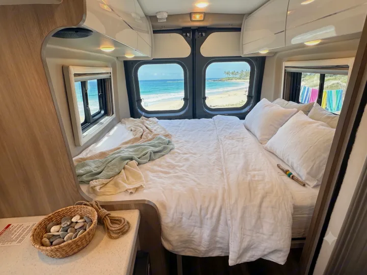 Experience the ultimate **RV rental** adventure: a cozy **camper van** interior featuring a comfortable bed and breathtaking **beach view**.. Thor Tellaro 2024