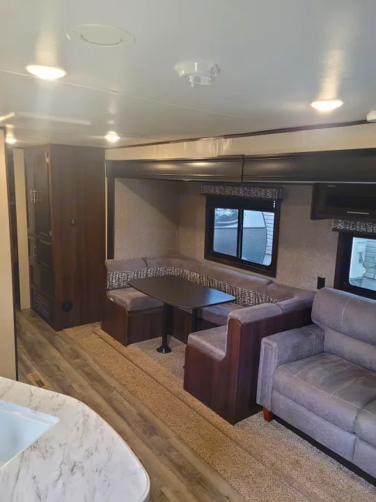RV rental interior: Modern living space with U-shaped dining booth, table, sofa, and kitchen view. Well-lit and cozy.. Jayco Jay Flight SLX 2019