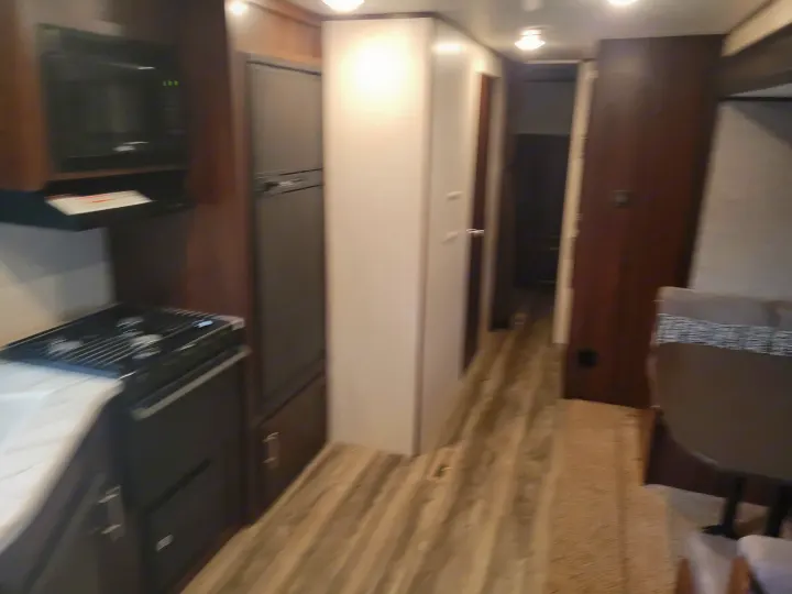 RV rental interior: a functional kitchen (microwave, stove, fridge), central hallway, and partial dining area visible on the right.. Jayco Jay Flight SLX 2019