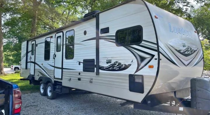 White travel trailer RV rental with mountain decals, parked on gravel at a wooded campsite, ready for your next trip.. Layton Layton Trailer 2014