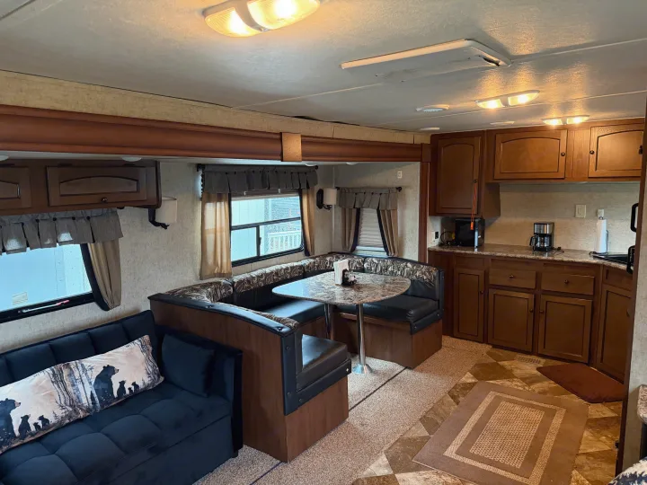 Comfortable RV rental interior featuring a living area with a sofa, a U-shaped dinette, and a full kitchen for travel comfort.. Layton Layton Trailer 2014