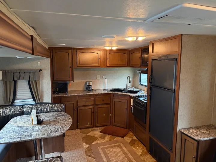 This RV rental shows a fully equipped kitchen and dinette with wood cabinets, fridge, stove, and bright lighting.. Layton Layton Trailer 2014