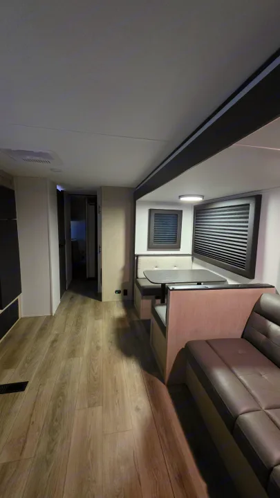 Modern RV rental interior: wood-look floor, dinette, and comfy sofa in a spacious living area, leading to rear rooms.. Forest River Shasta I-5 2025