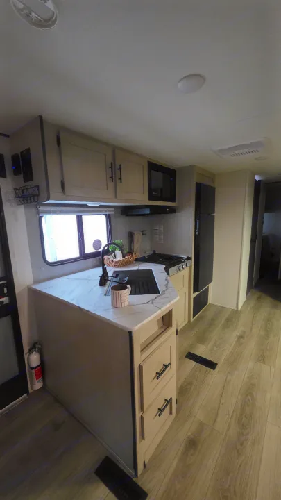 Clean rv rental kitchen interior, featuring light wood cabinets, sink, stove, microwave, fridge, and wood-look flooring.. Forest River Shasta I-5 2025