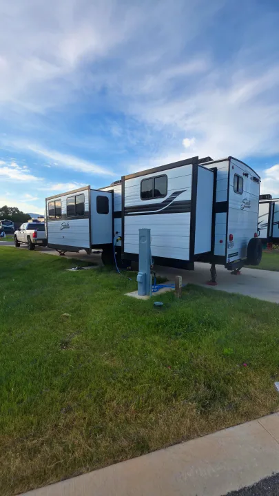 An RV rental, a white Shasta travel trailer, parked at campsite 314 with a pickup, showing extended slides and hookups.. Forest River Shasta I-5 2025