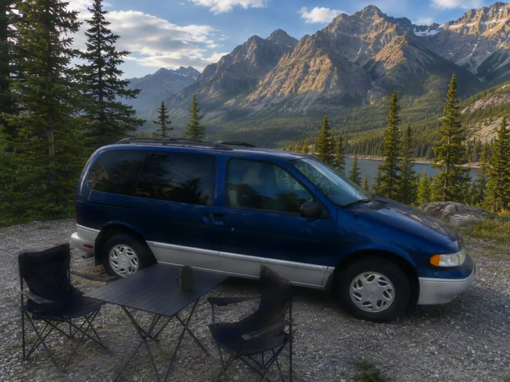 An RV rental minivan is parked at a scenic mountain lake campsite. Camping chairs and table set up for outdoor enjoyment.. Mercury Villager 1997