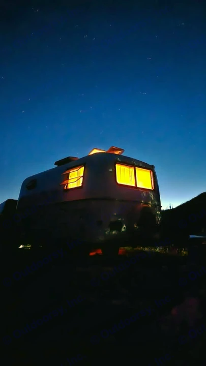 Experience starry nights in this cozy **rv rental**! Vintage camper glows warmly against the deep blue, star-filled sky.. Scamp Scamp Trailer 2004