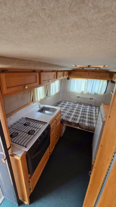 RV rental interior: compact kitchen (stove, sink), cozy bed with plaid cushions, and wood cabinets for your road trip.. Scamp Scamp Trailer 2004
