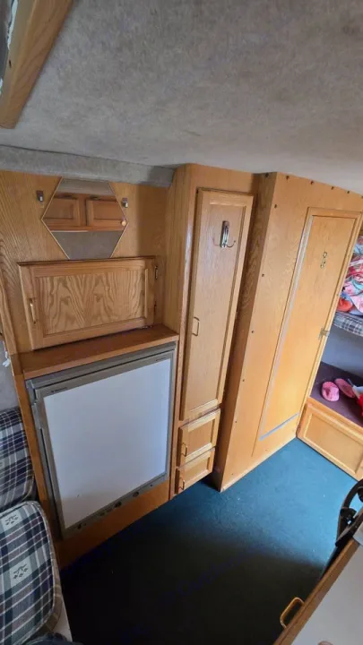 Cozy rv rental interior with light wood paneling, a refrigerator, storage cabinets, and a bunk bed. Plaid seating and carpeted floor.. Scamp Scamp Trailer 2004