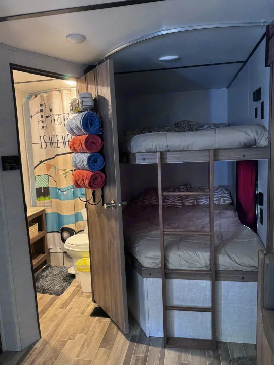 This RV rental interior features comfortable bunk beds on the right, and a compact bathroom with shower on the left.. Crossroads RV Zinger Lite 2021