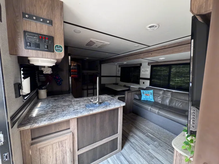 Bright RV rental interior: kitchen with control panel, living room with sofa, dinette, and visible bunk beds in back.. Crossroads RV Zinger Lite 2021
