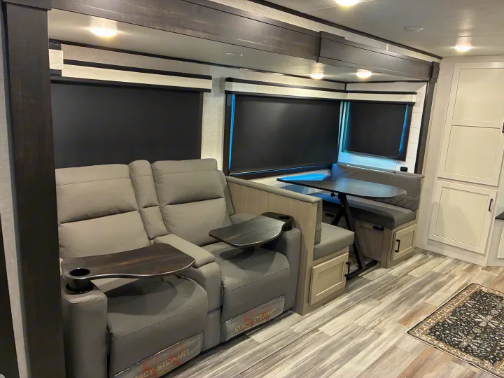 This modern RV rental interior features comfortable gray recliners with swing-out tables and a built-in dinette.. Jayco Jay Feather 2024