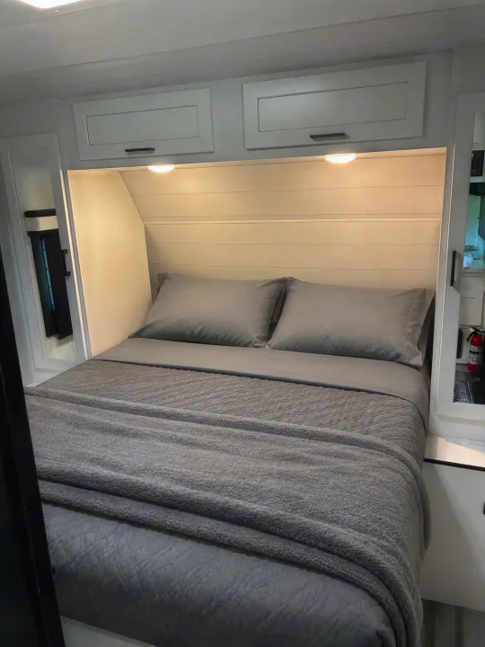 This RV rental offers a cozy, modern bedroom with a gray bed, overhead cabinets, and lighting for a relaxing stay.. Jayco Jay Feather 2024