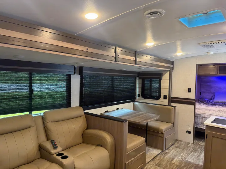 Cozy rv rental interior featuring tan recliners, a dining booth, and a glimpse of the private bedroom.. Crossroads RV Sunset Trail Super Lite 2022