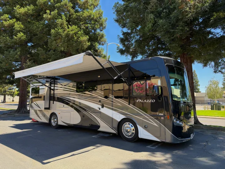Sleek Palazzo motorhome rv rental, black and tan with an extended awning, parked under shade trees. Ready for adventure.. Thor Palazzo 2017