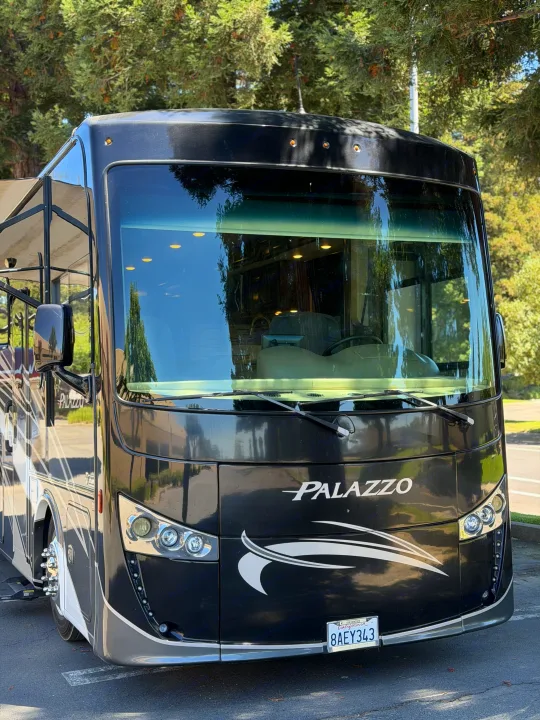 Front view of a sleek black Palazzo RV with gray accents, California license plate, and bright headlights, ideal for an rv rental.. Thor Palazzo 2017