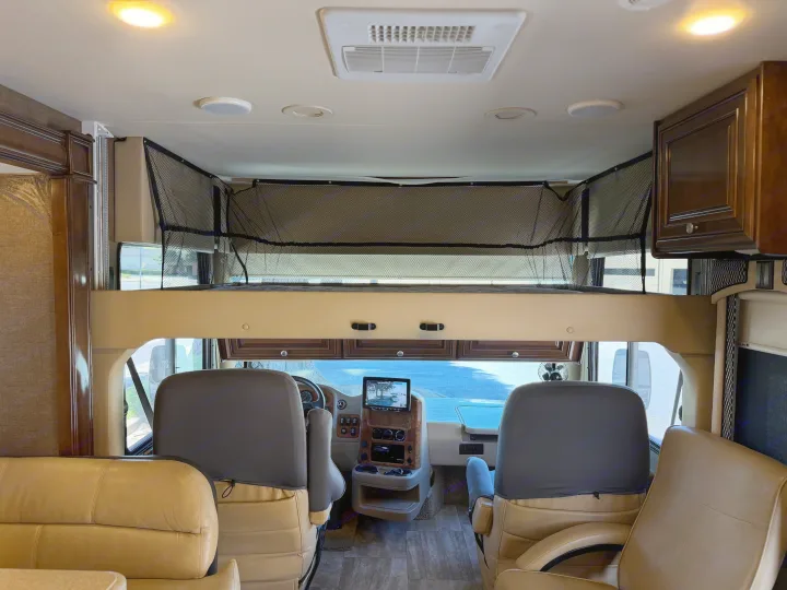 This RV rental's interior boasts a comfortable cockpit, dashboard screen, and an overhead bunk bed with safety netting.. Thor Palazzo 2017