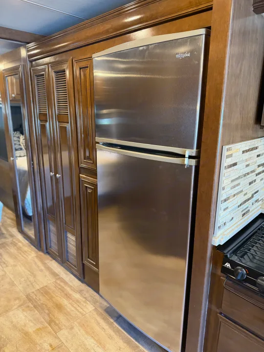 This RV rental interior features a stainless Whirlpool fridge, dark wood cabinets, tile backsplash, and a stovetop.. Thor Palazzo 2017