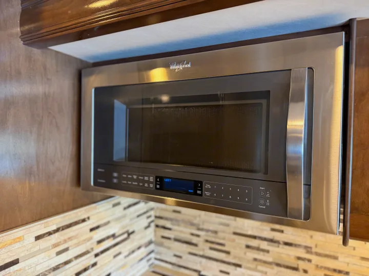 Stainless steel Whirlpool microwave in an RV rental kitchen, showing its controls, digital display, and tile backsplash.. Thor Palazzo 2017