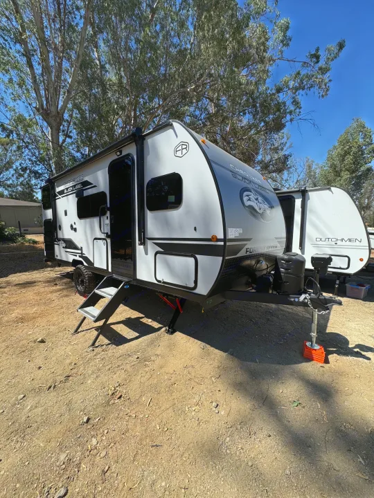 Grey and black Forest River Cherokee travel trailer and another RV on a dirt lot, parked under trees, ready for an rv rental trip.. Forest River Cherokee Wolf Pup 2026