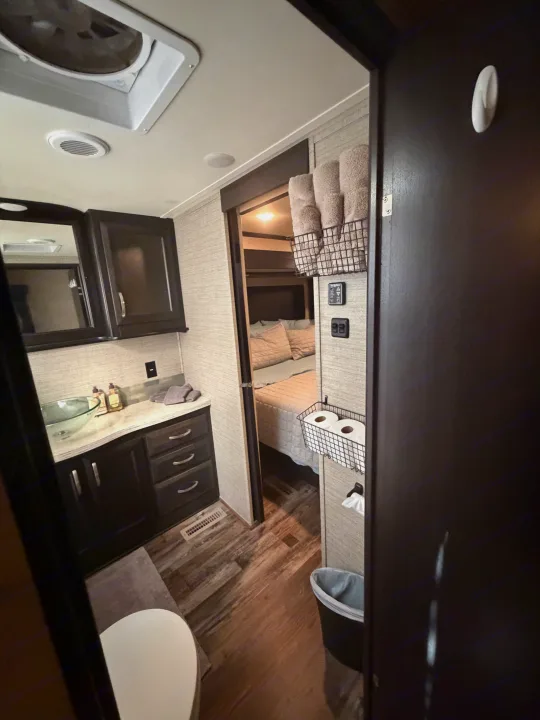 View inside an RV rental: a compact bathroom with a sink, mirror, and toilet, offering a glimpse into the adjacent bedroom.. Denali Denali Fifth Wheel 2017