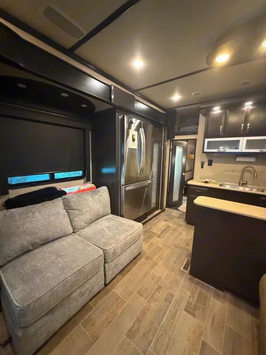 Spacious RV rental interior featuring a modern kitchen with stainless steel appliances, a comfortable gray sectional sofa, and wood-look tile flooring.. Denali Denali Fifth Wheel 2017