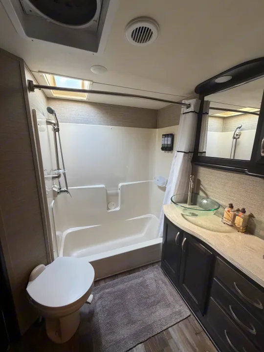 This rv rental bathroom features a compact shower, toilet, and vanity with a glass sink, along with a ceiling vent.. Denali Denali Fifth Wheel 2017