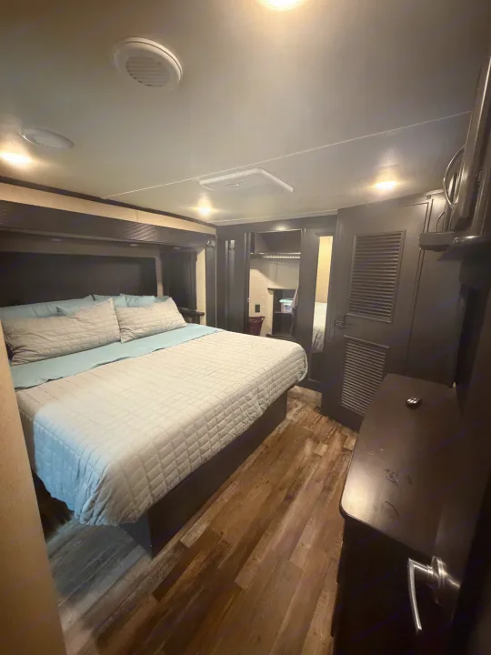 An inviting RV rental bedroom with a large bed, light blue bedding, and dark wood cabinetry. Wood-look floors complete the modern interior.. Denali Denali Fifth Wheel 2017