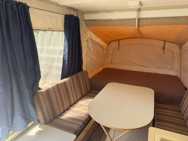 Cozy RV rental pop-up camper interior features a dinette, bed, and bright windows, great for camping.. Coleman Grand Tour Shenandoah 1987