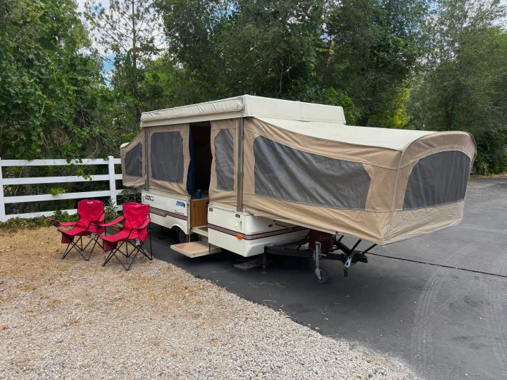 Coleman pop-up RV rental fully set up with red camping chairs, ready for an outdoor adventure among green trees.. Coleman Grand Tour Shenandoah 1987