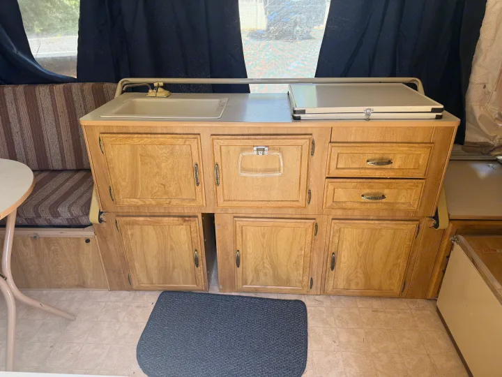 RV rental pop-up camper kitchen: sink, covered stove, wood cabinets, and seating. Camping adventure ready!. Coleman Grand Tour Shenandoah 1987